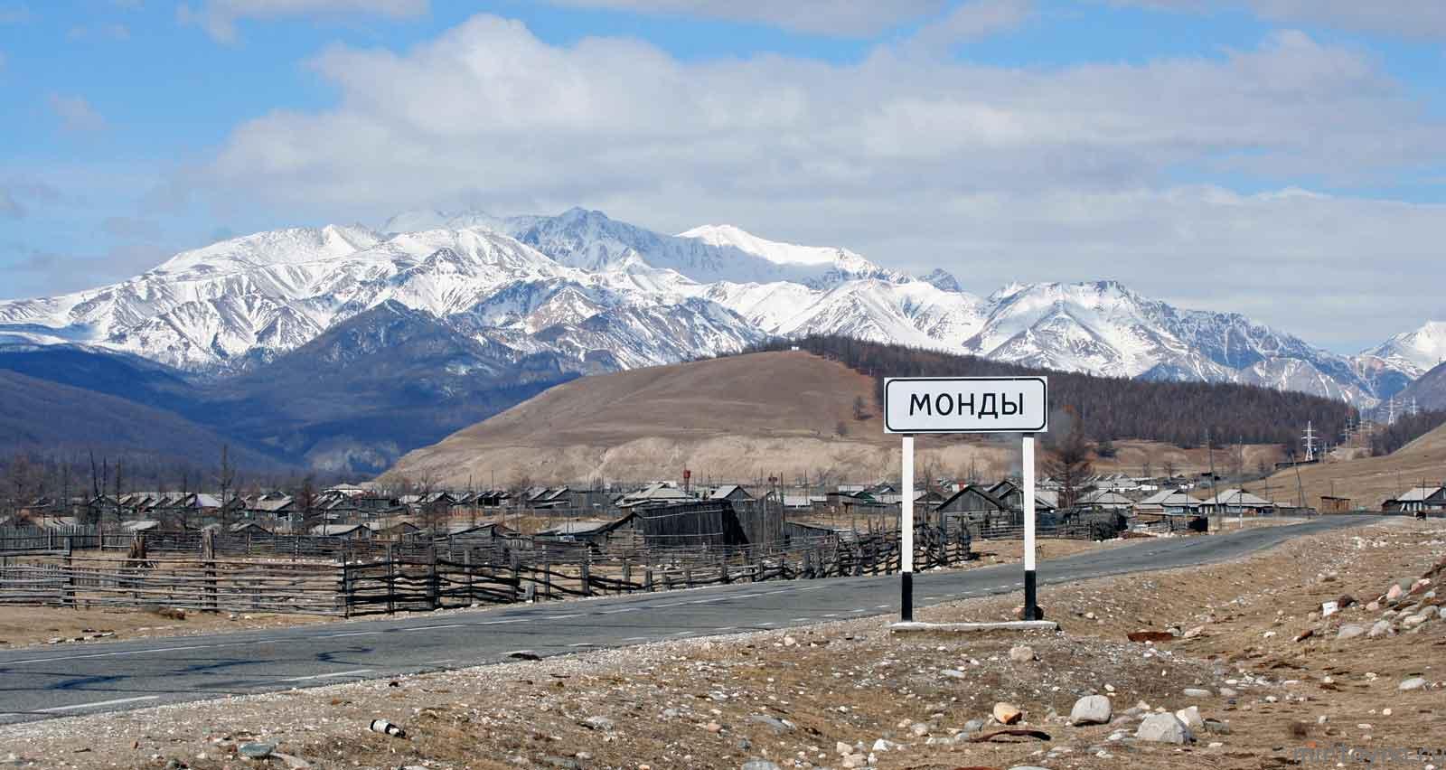 Дорожный знак с надписью 'Монды' на фоне горного пейзажа и поселка.
